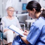 Nurse writing prescription for disabled senior woman in wheelchair after medical examination. Recovery treatment, help for disabled people. Elderly assistance